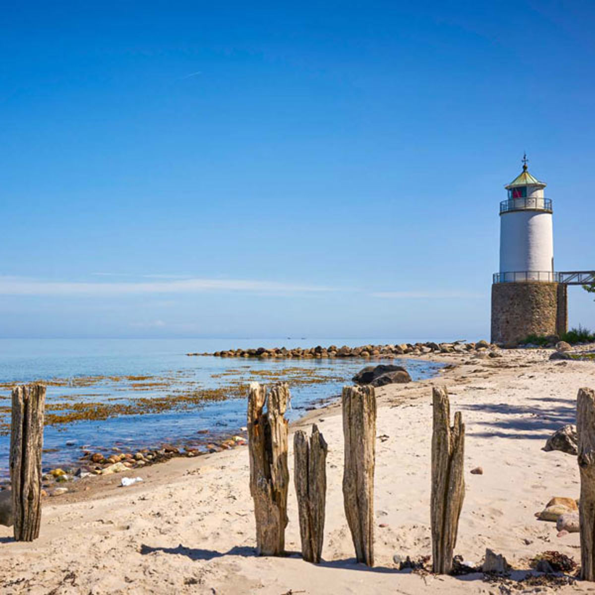 A lighthouse is visible in the background on a sandy beach at Als.