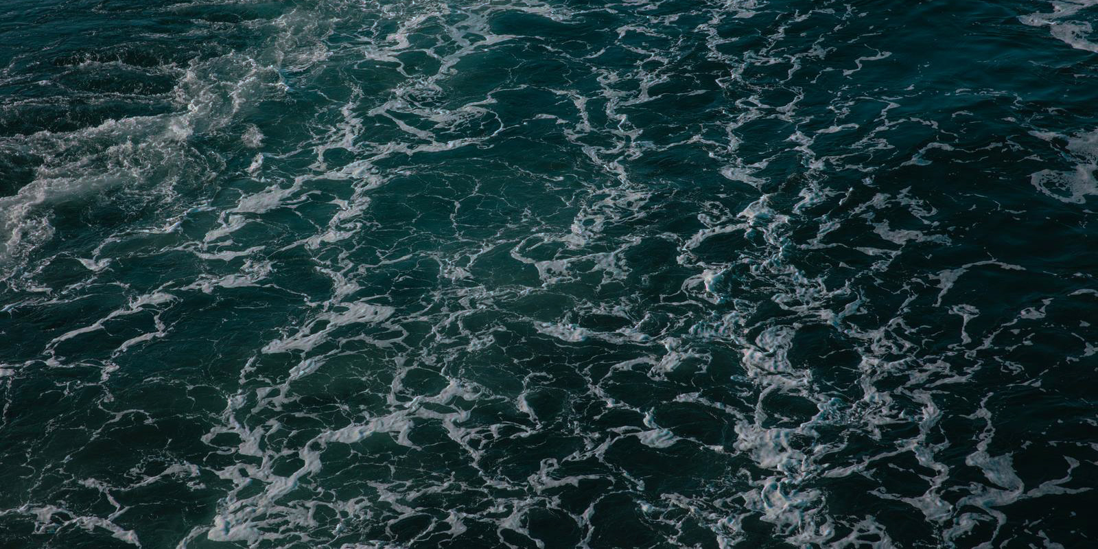 Waves with white foam on the open sea viewed from above, displaying the water's dynamic patterns.