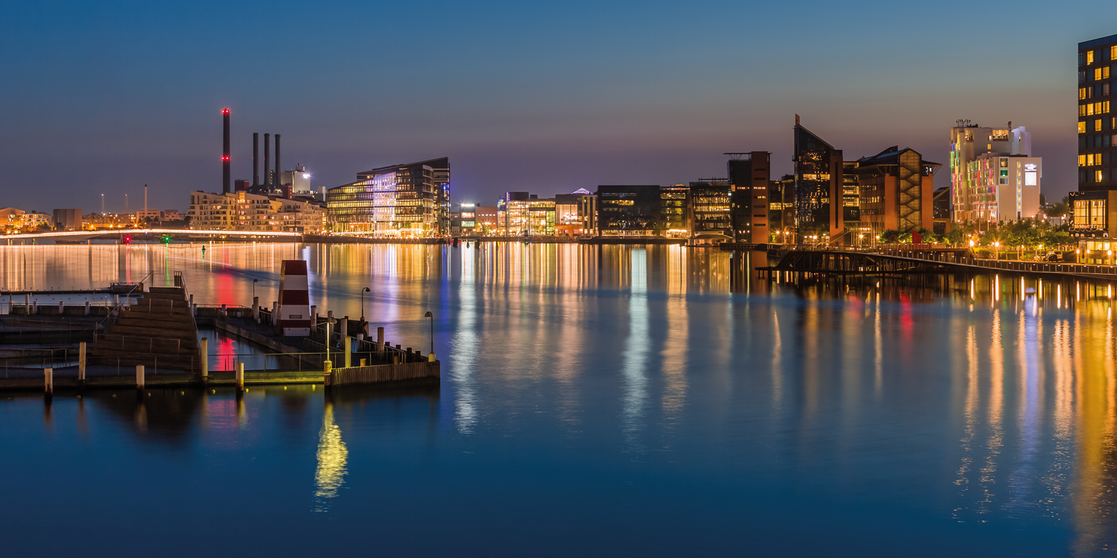 Modern buildings at Aarhus waterfront at dusk with illuminated reflections in the water.