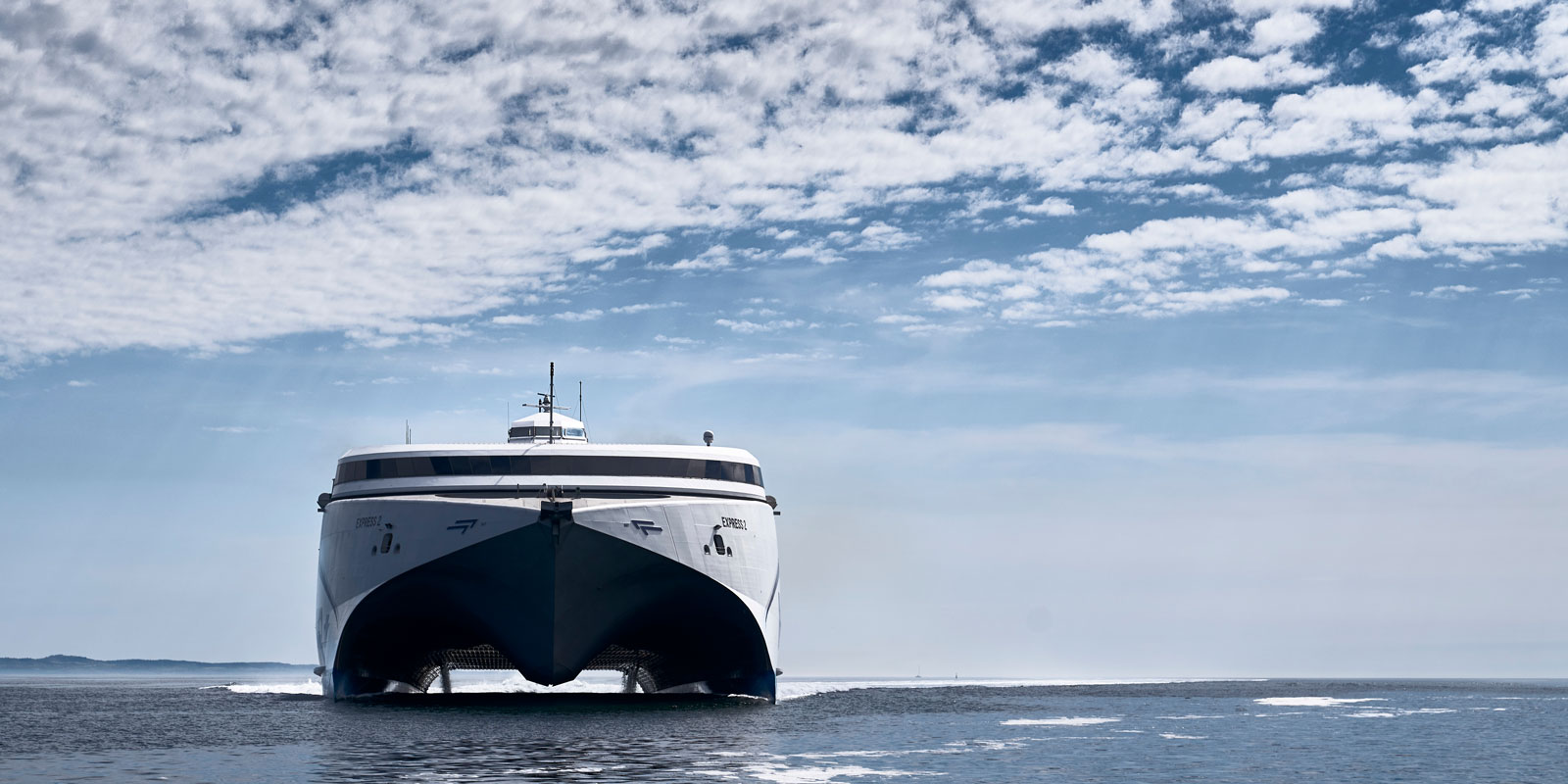 Multihull ferry cruising through the sea with a clear blue sky above.