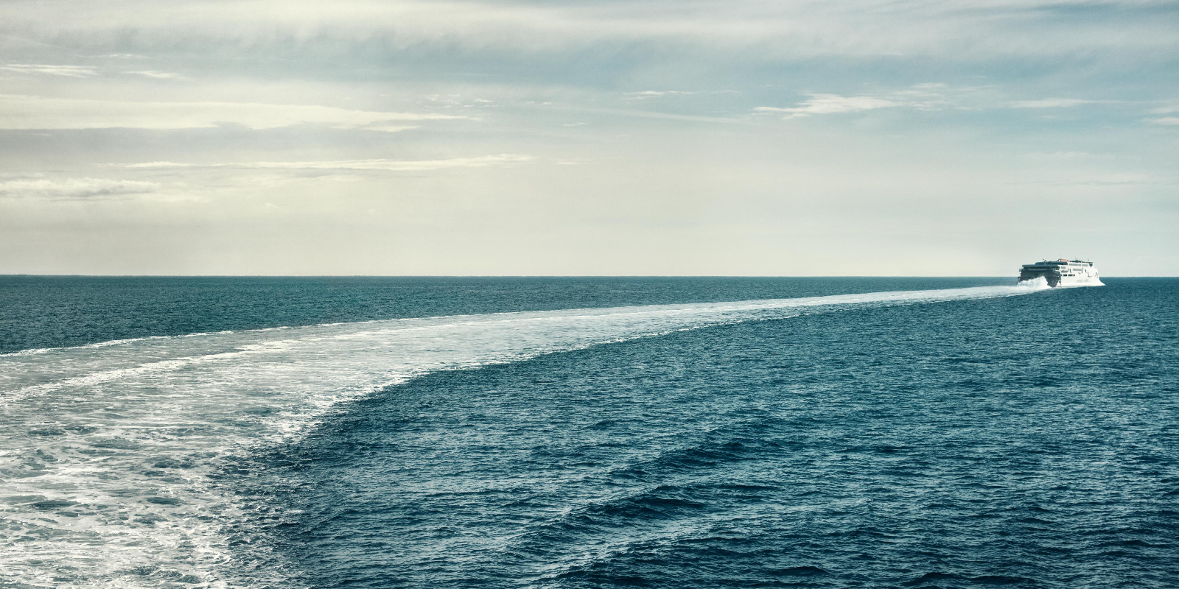 Molslinjen ferry Express 3 sails towards the horizon across the open sea with clear, blue water.