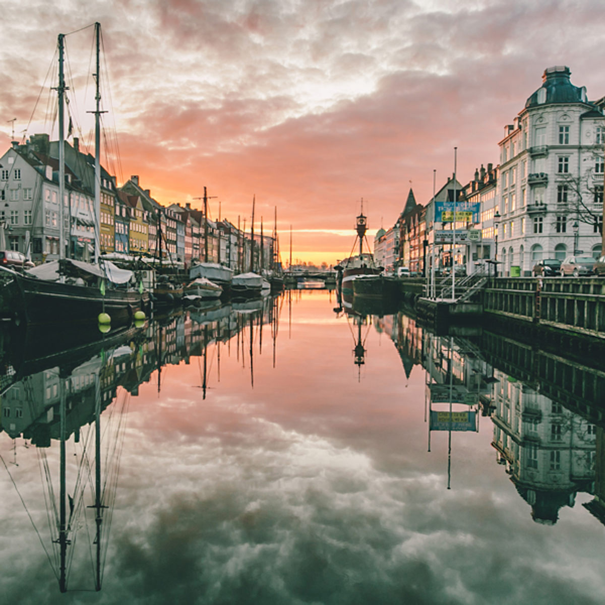 Nyhavn canal in Copenhagen at sunset with reflections of houses and ships in the water.