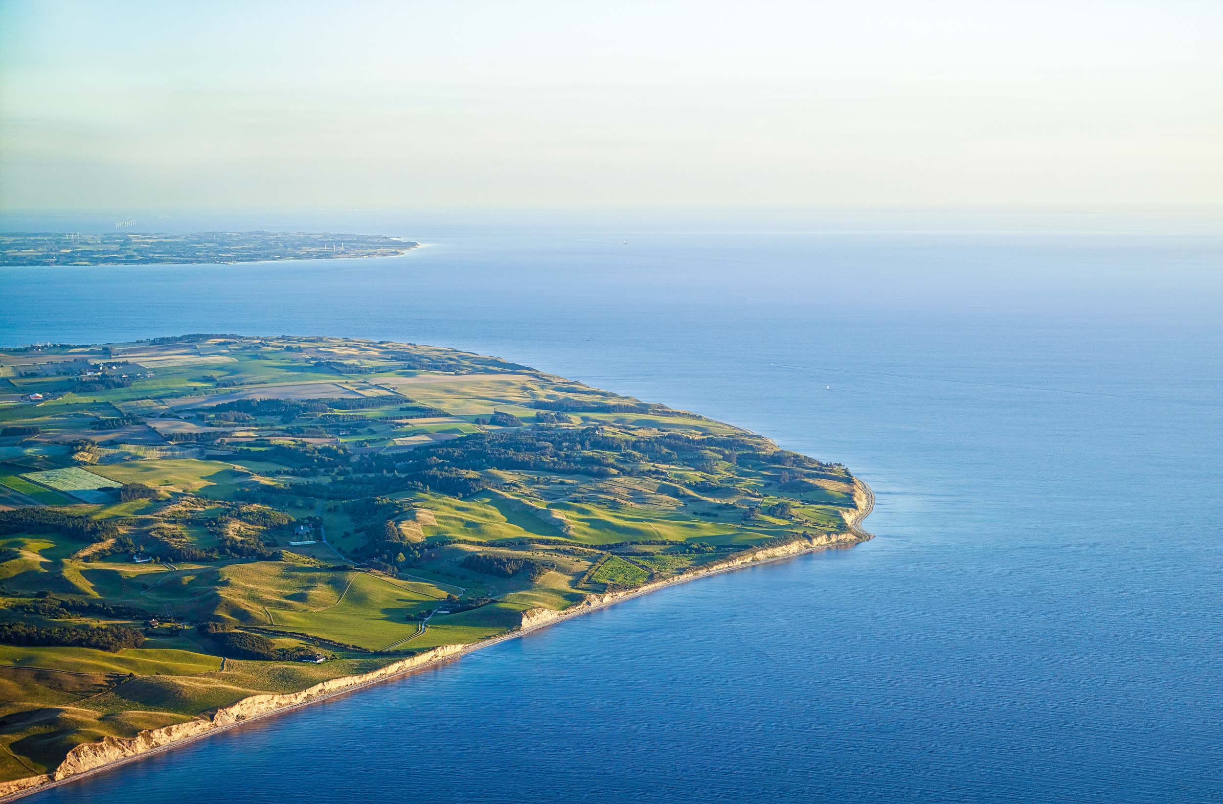 Aerial view of Samsoe island's coastline with clear blue waters and lush green landscape.