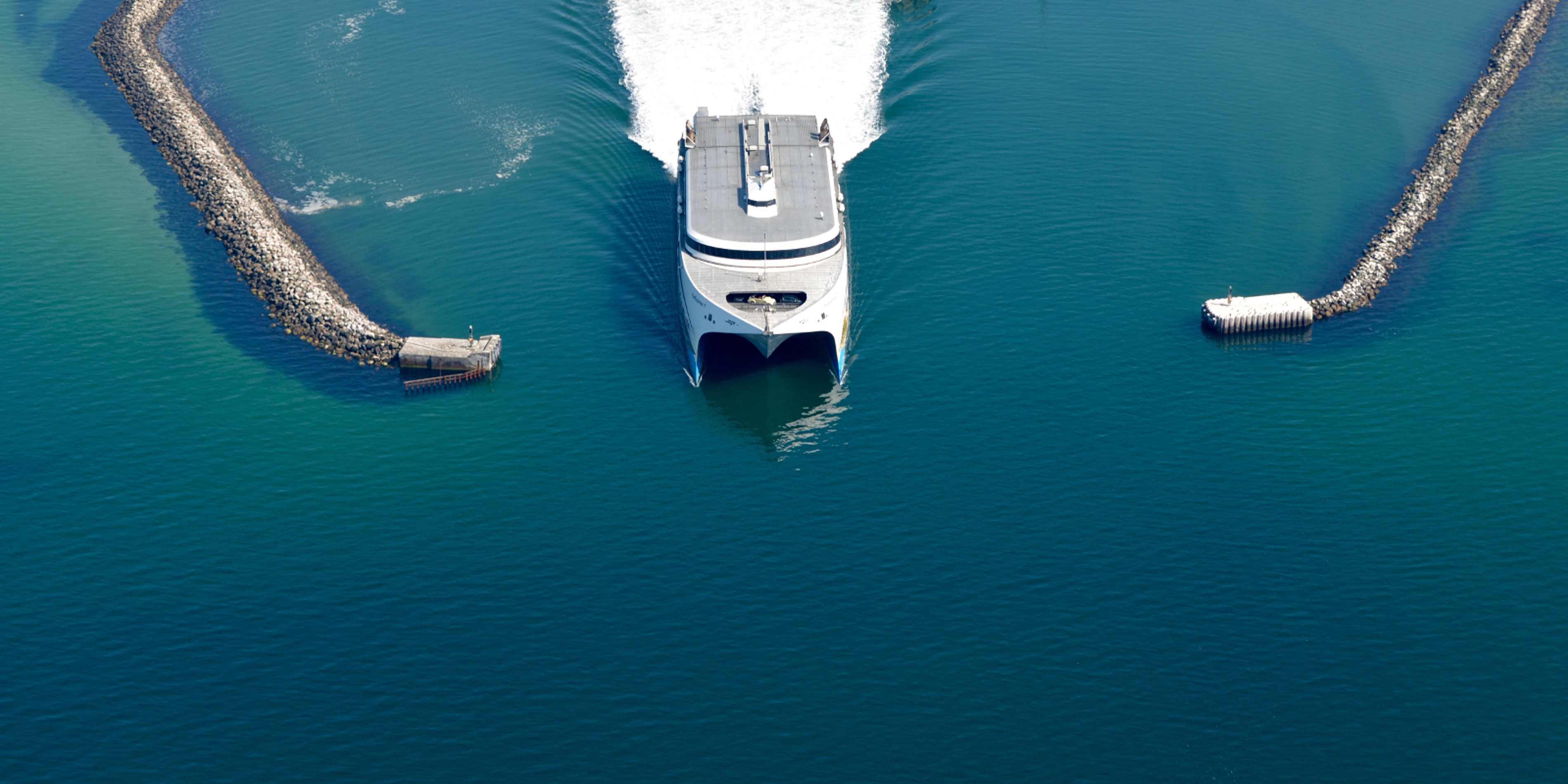Molslinjen ferry departs Odden harbor in sunlight, viewed from an aerial view.