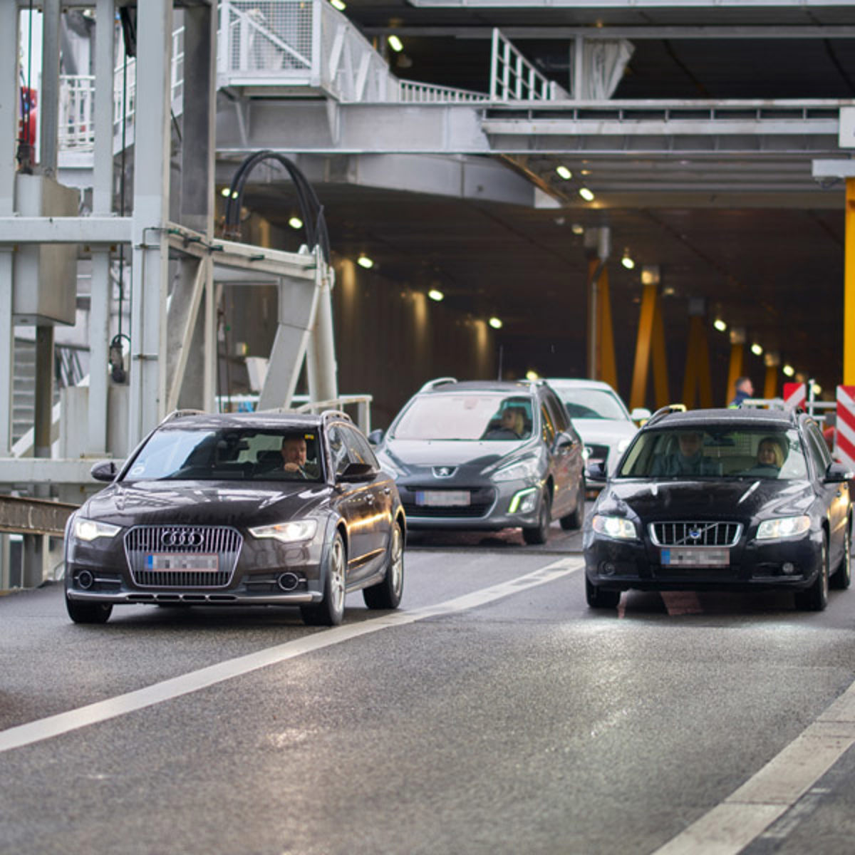 Cars leaving the ferry at harbor, focusing on a black car exiting in heavy traffic.