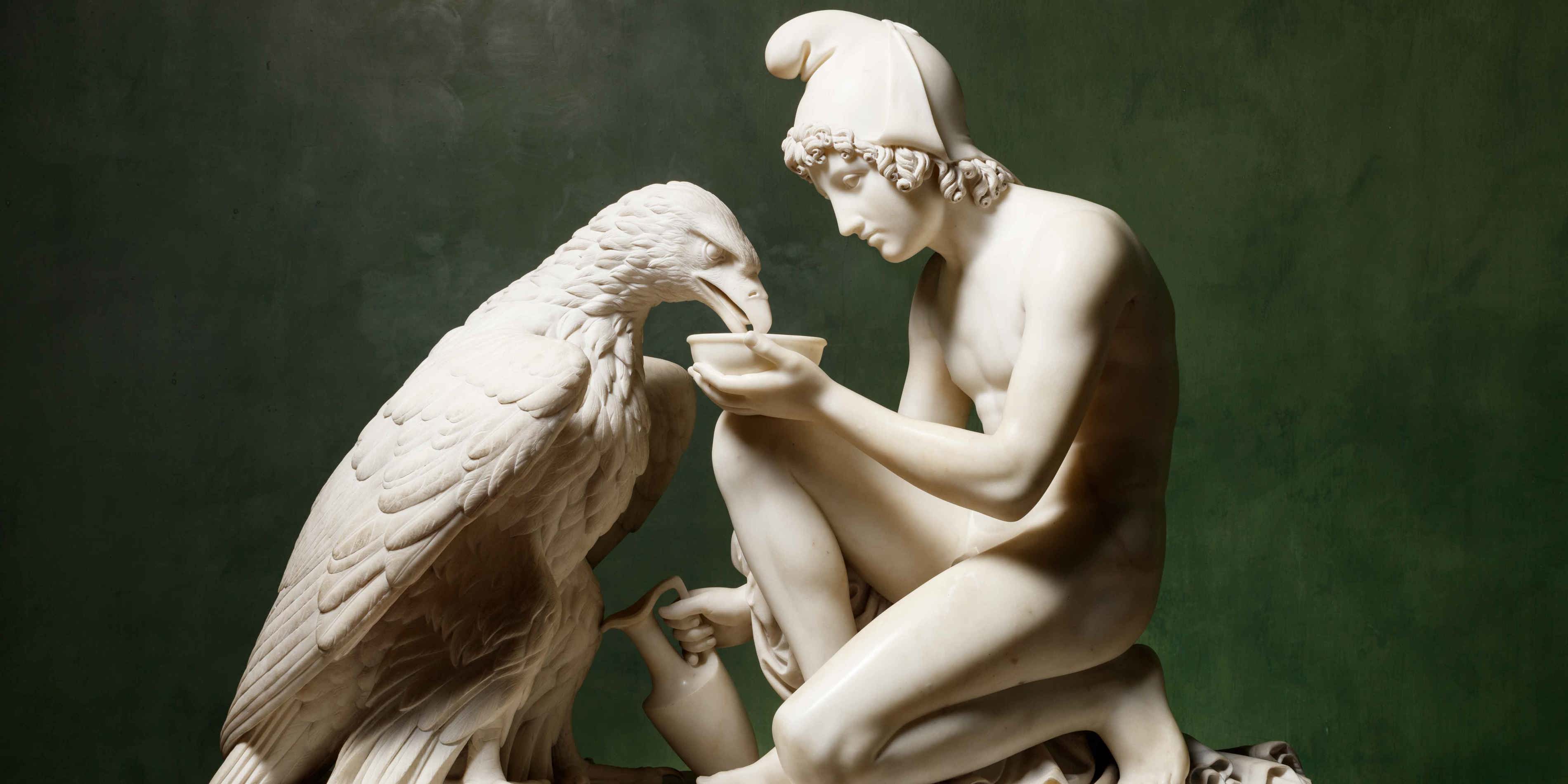 Statue of ancient Greek man and eagle made of white marble, highlighting artistic details.