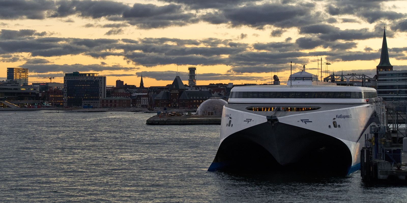 Molslinjen ferry docked at harbor during sunset with city skyline in the background.
