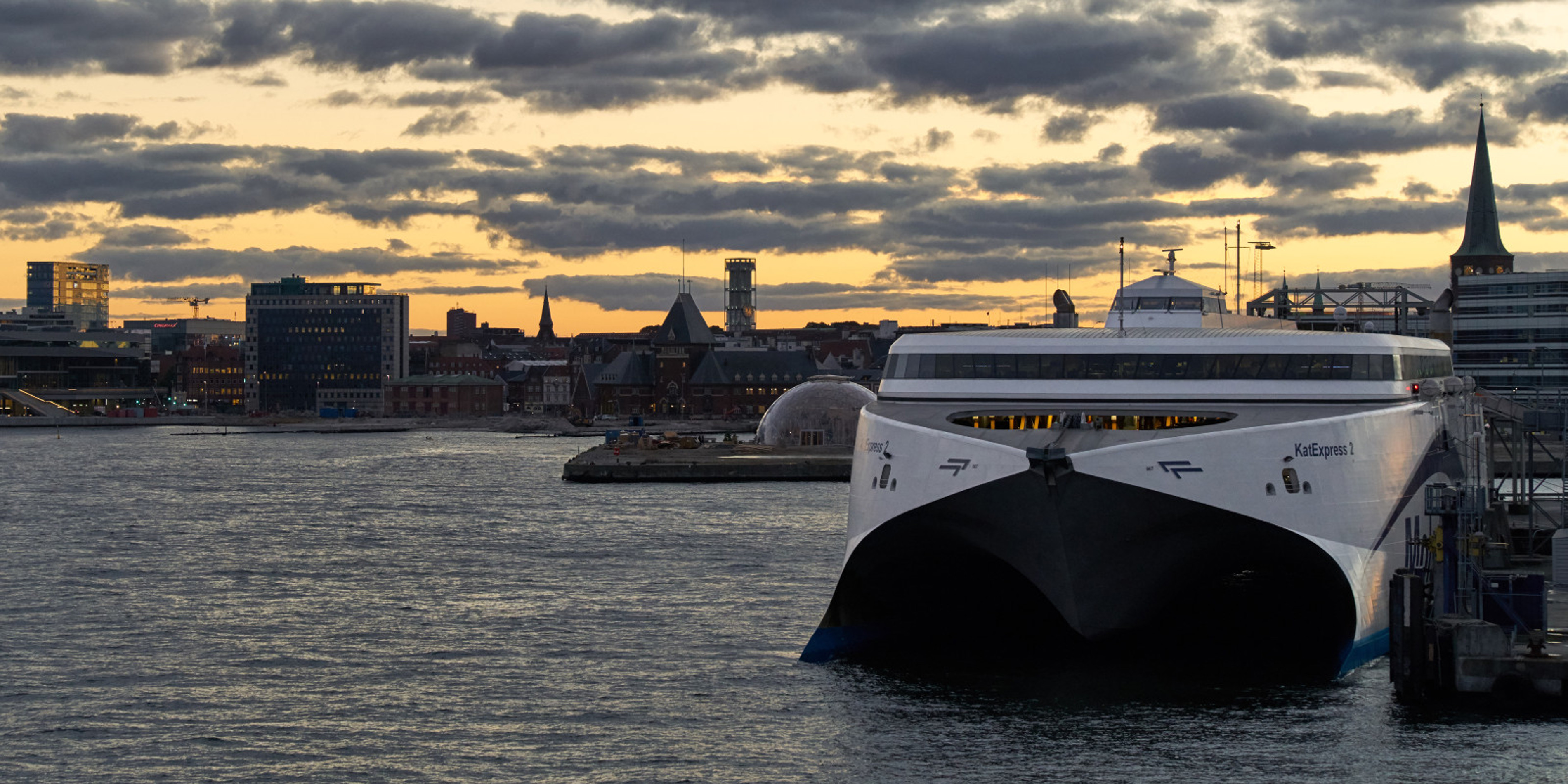 Molslinjen ferry docked at harbor during sunset with city skyline in the background.