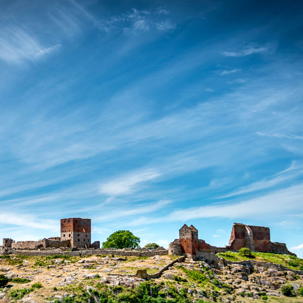 A rocky hilltop with ruins under a clear blue sky and small white clouds.