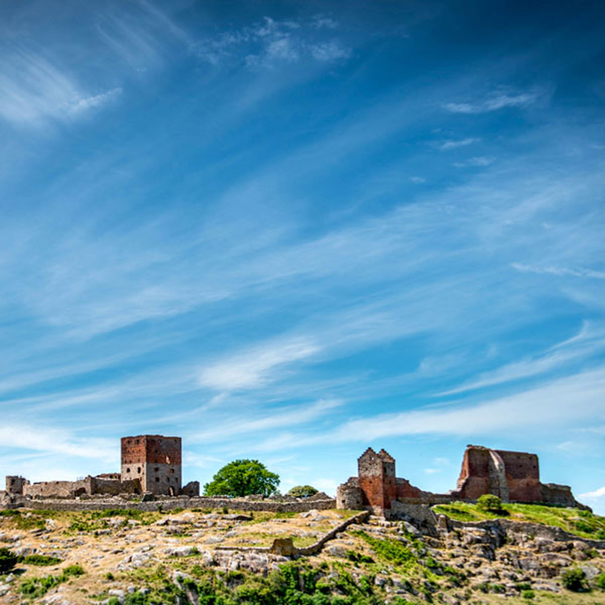A rocky hilltop with ruins under a clear blue sky and small white clouds.