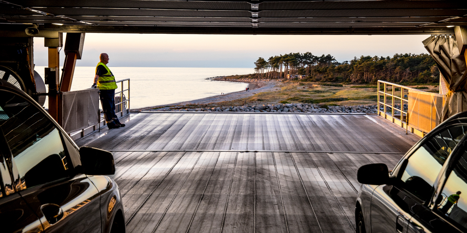 View from the car deck of the Odden ferry, overlooking sea, beach, and greenery at sunset.