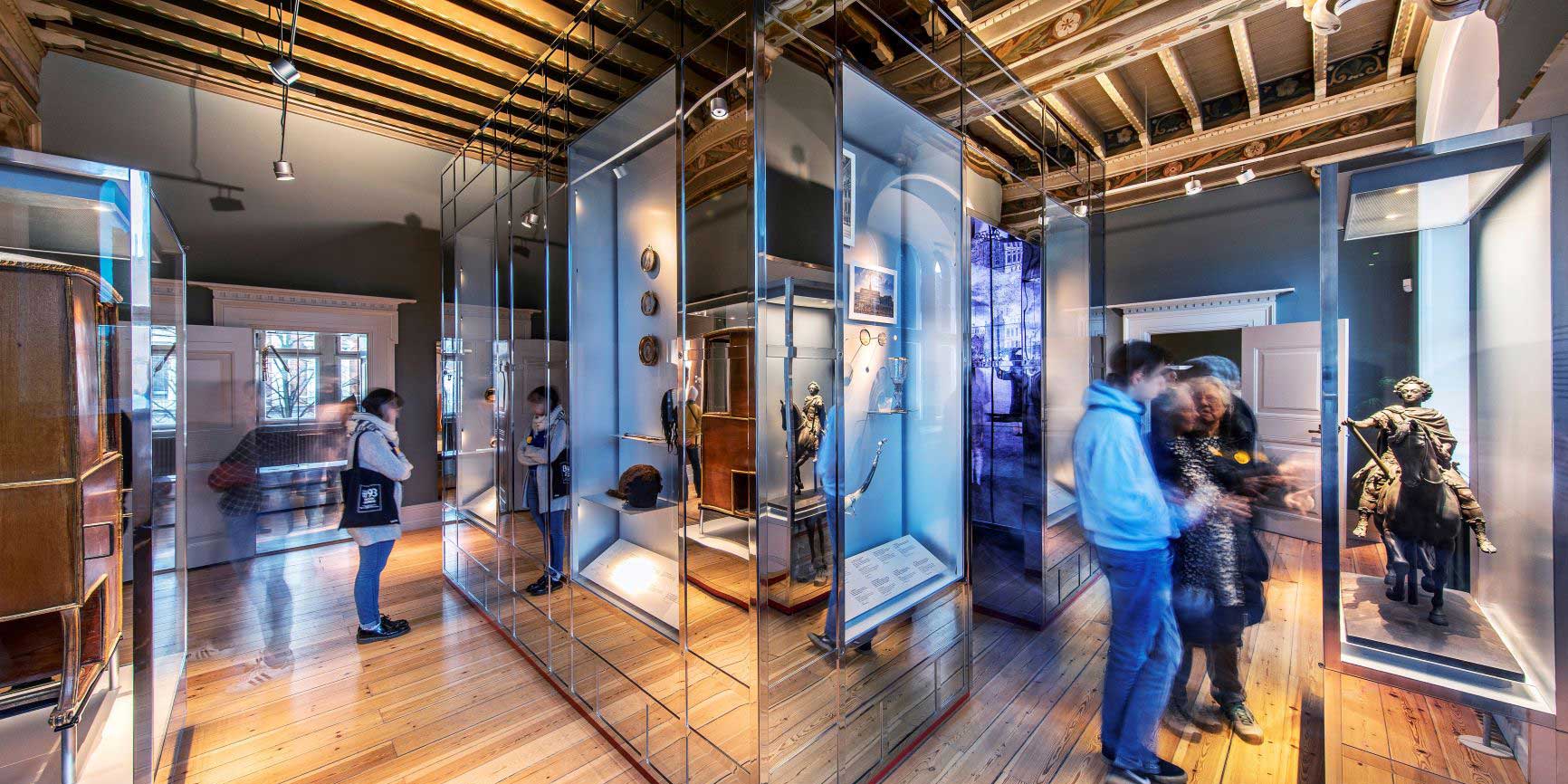Visitors observing exhibitions in modern glass display cases on a historical wooden floor at Copenhagen Museum.