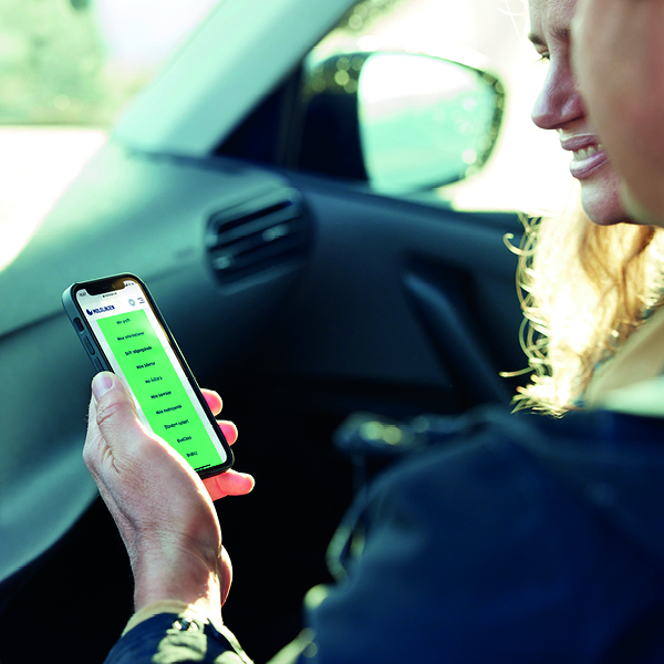Person using smartphone with green screen in car passenger seat during daylight.