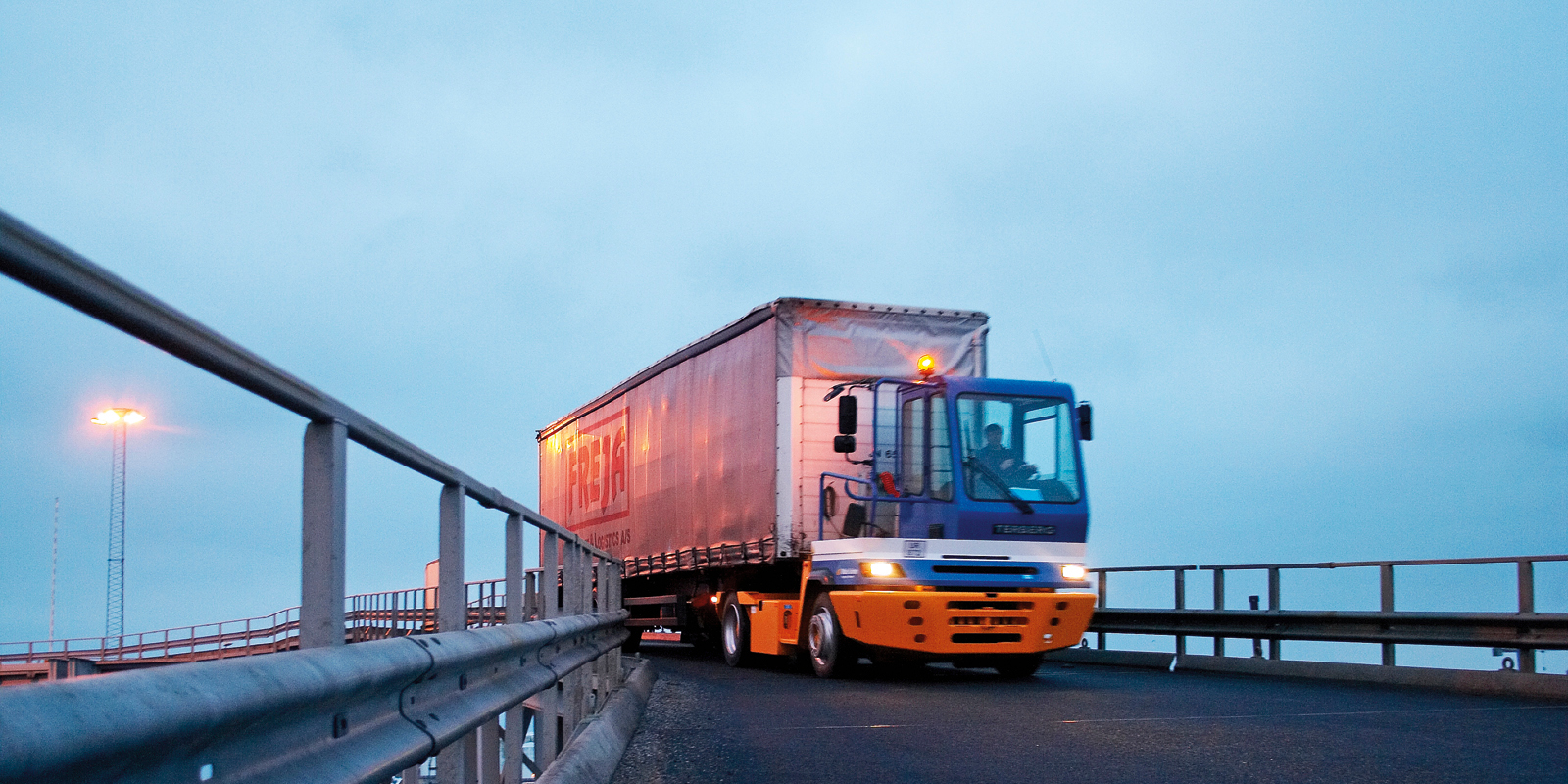 Container truck driving onto ferry under clear blue sky, viewed in profile.