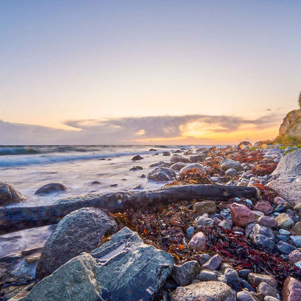 A rocky beach on Samsø with the sun setting in the background, highlighting the serene landscape.